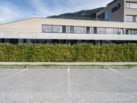 there is a parking lot with a large building and hedges in the background next to a street