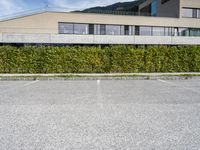 there is a parking lot with a large building and hedges in the background next to a street