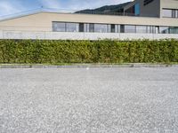 there is a parking lot with a large building and hedges in the background next to a street