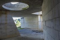 a tunnel with concrete walls and an open circular window for the sun to shine down on