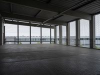 an industrial space with a very large window looking out to the sea and some cars in the lot