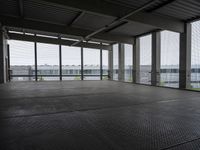 an industrial space with a very large window looking out to the sea and some cars in the lot