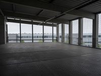 an industrial space with a very large window looking out to the sea and some cars in the lot