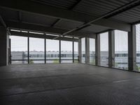 an industrial space with a very large window looking out to the sea and some cars in the lot