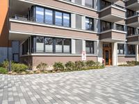 two brown building with large windows and no door are in a driveway in front of some bushes