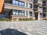 two brown building with large windows and no door are in a driveway in front of some bushes