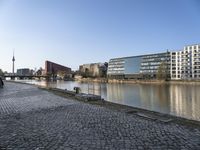 a large stone road with buildings and people riding bikes next to a river and two tall buildings