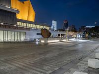 an empty courtyard with a stone bench outside of it, at night with buildings in the background