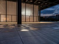 a sidewalk with a window and some lights outside it at dusk by a clock tower