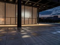 a sidewalk with a window and some lights outside it at dusk by a clock tower