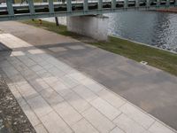 a paved sidewalk along the bank next to some water and benches and trees in the shade