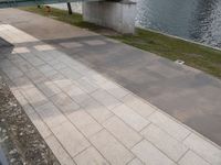 a paved sidewalk along the bank next to some water and benches and trees in the shade