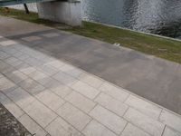 a paved sidewalk along the bank next to some water and benches and trees in the shade