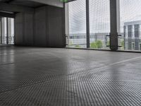 large open building with a metal mesh floor covering the floor and ceiling, looking out onto large cityscape outside