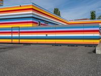 an empty parking lot painted brightly stripes on the wall of the building and sky as well as stones