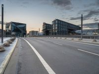 empty road on the edge of an open highway with modern buildings behind it at dusk