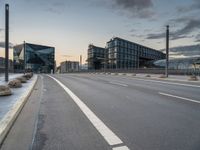 empty road on the edge of an open highway with modern buildings behind it at dusk