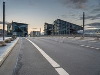 empty road on the edge of an open highway with modern buildings behind it at dusk