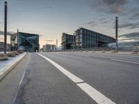 empty road on the edge of an open highway with modern buildings behind it at dusk