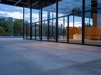 a building with glass walls and a large bench in the back room surrounded by trees