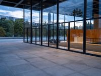 a building with glass walls and a large bench in the back room surrounded by trees