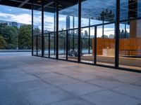 a building with glass walls and a large bench in the back room surrounded by trees