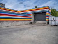 an empty parking lot painted brightly stripes on the wall of the building and sky as well as stones