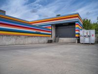 an empty parking lot painted brightly stripes on the wall of the building and sky as well as stones