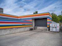 an empty parking lot painted brightly stripes on the wall of the building and sky as well as stones