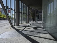 the sun shines through a building into a street lined with tall glass panels and concrete