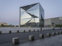 a tall building near a sidewalk in front of an office building that is glass - walled and has geometric structures and lines