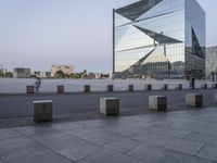 a tall building near a sidewalk in front of an office building that is glass - walled and has geometric structures and lines