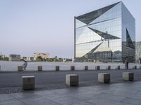 a tall building near a sidewalk in front of an office building that is glass - walled and has geometric structures and lines