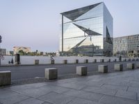 a tall building near a sidewalk in front of an office building that is glass - walled and has geometric structures and lines