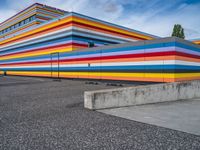 an empty parking lot painted brightly stripes on the wall of the building and sky as well as stones