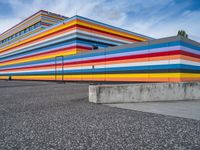 an empty parking lot painted brightly stripes on the wall of the building and sky as well as stones