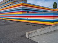 an empty parking lot painted brightly stripes on the wall of the building and sky as well as stones