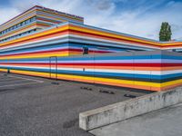 an empty parking lot painted brightly stripes on the wall of the building and sky as well as stones