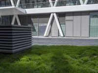 a sculpture sitting in the grass near an office building with multiple angles to each other