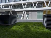 a sculpture sitting in the grass near an office building with multiple angles to each other