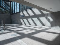 the sun casts a long shadow through some glass walls in an empty building lobby on a sunny day