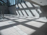 the sun casts a long shadow through some glass walls in an empty building lobby on a sunny day