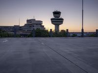 a concrete parking lot with an air control tower in the background and a sunset behind them