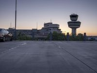 a concrete parking lot with an air control tower in the background and a sunset behind them