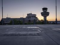 a concrete parking lot with an air control tower in the background and a sunset behind them