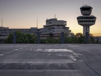 a concrete parking lot with an air control tower in the background and a sunset behind them