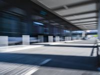 blurred image of an airport with a train passing by and people standing at the curb waiting area