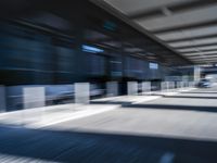 blurred image of an airport with a train passing by and people standing at the curb waiting area