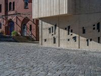 cobblestone driveway surrounded by modern buildings on sunny day with sun reflecting onto the windows