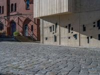 cobblestone driveway surrounded by modern buildings on sunny day with sun reflecting onto the windows